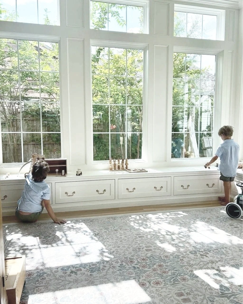 A bright kids study with expansive white millwork windows and a built-in window seat, demonstrating optimal natural light for a learning space. Design by Studio McGee.