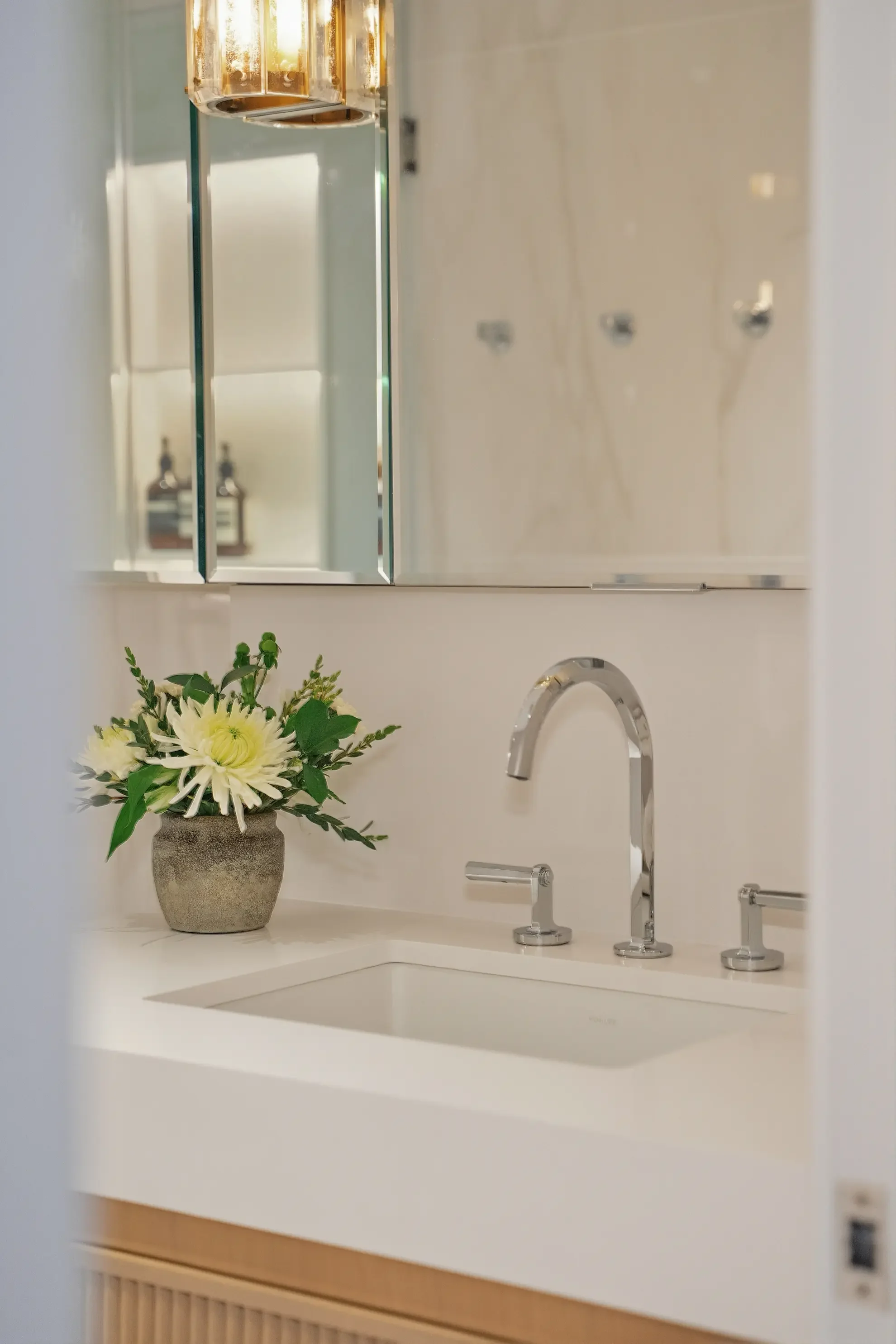 Luxury transitional bathroom in Toronto by Claire Design Studio, featuring a custom fluted wood vanity, white stone countertop, and two elegant pillar-style crystal pendant lights reflected in a mirrored medicine cabinet.