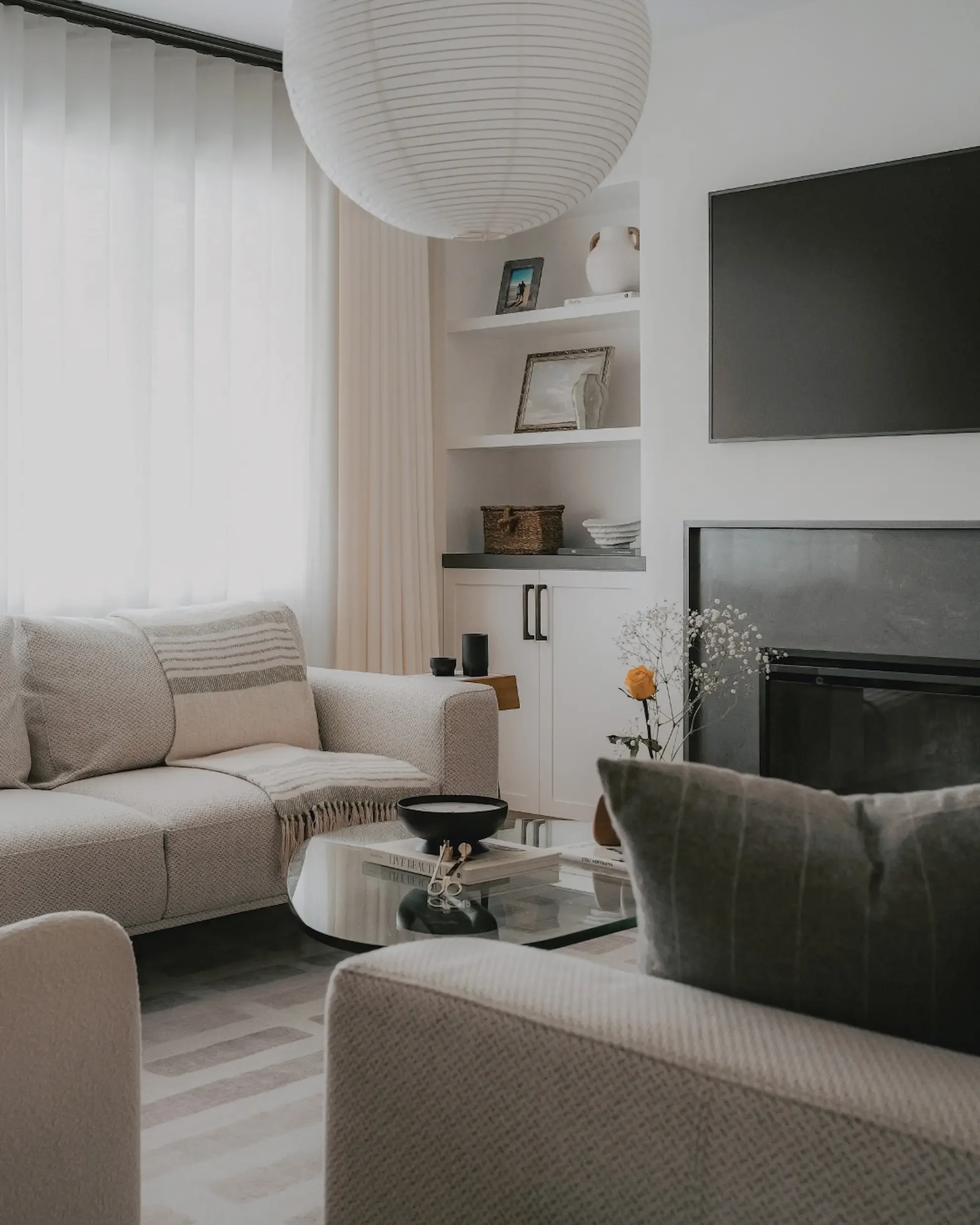 Modern living room interior in Toronto by Claire Design Studio, featuring a textured light grey sofa, a minimalist globe pendant light, and sheer white curtains filtering natural light.