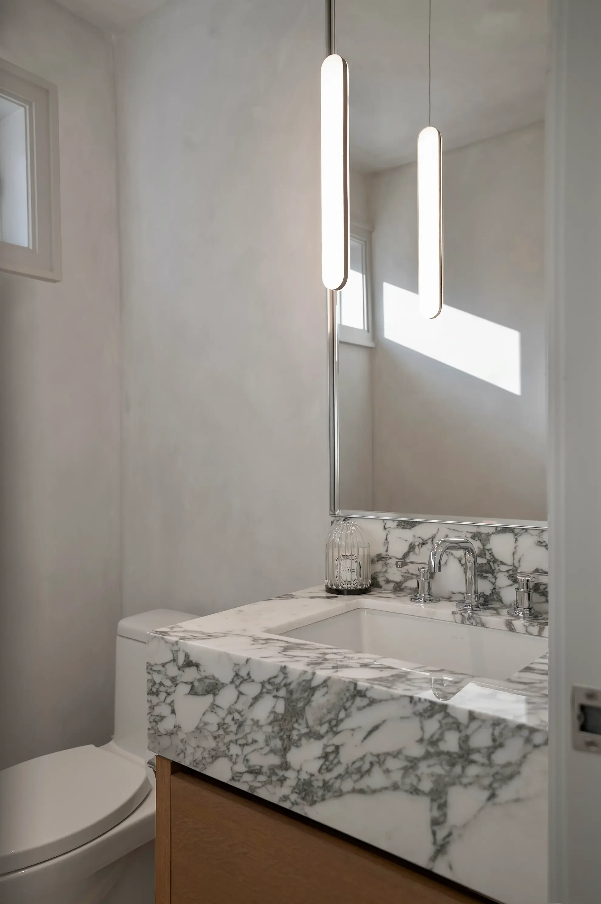 Luxury powder room in Toronto designed by Claire Design Studio, featuring a custom thick-edge marble vanity with dramatic veining, modern minimalist pendant lighting, and a sleek chrome faucet reflected in a large mirror.