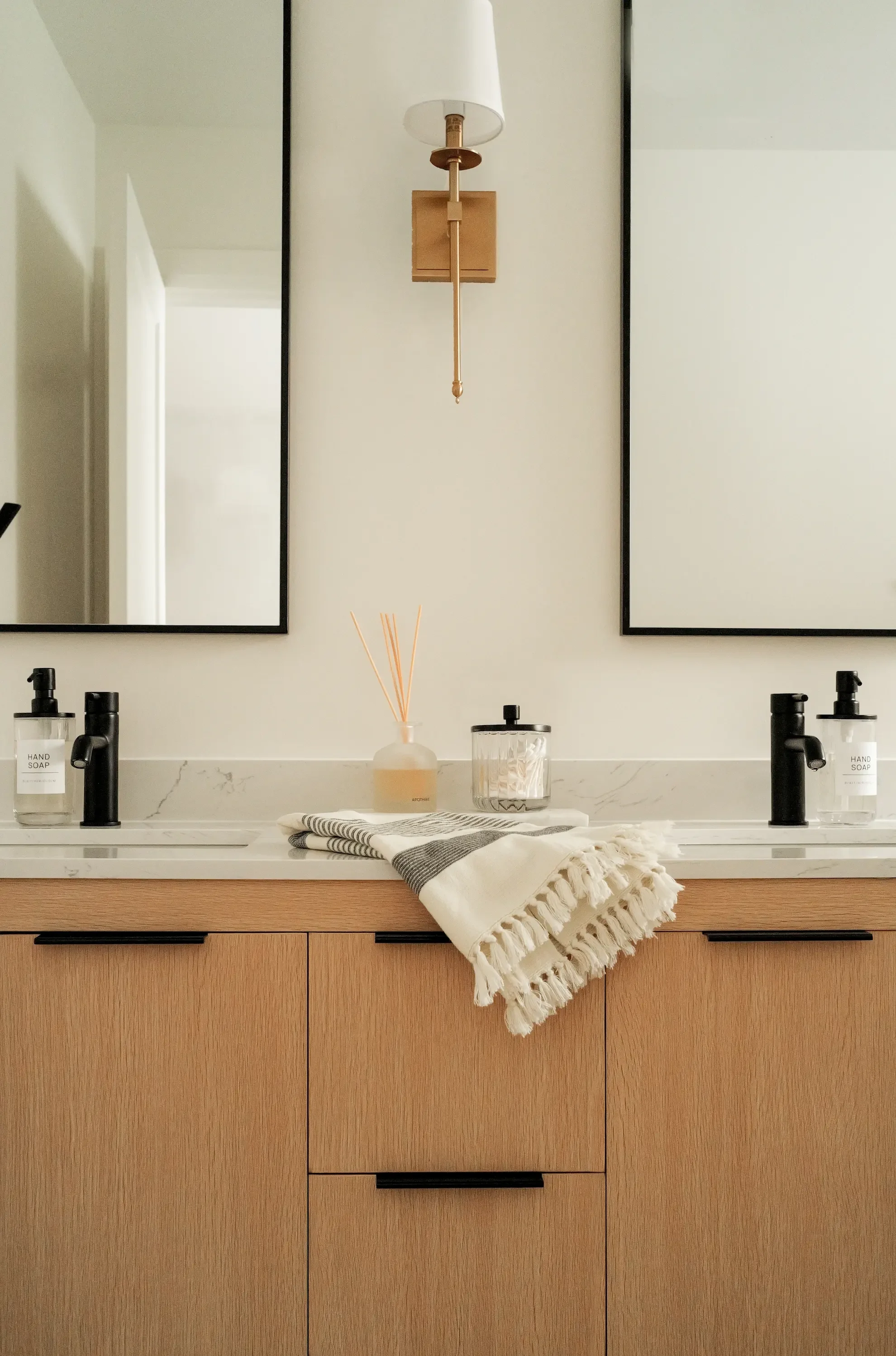 Toronto designed by Claire Design Studio, featuring light oak cabinetry, matte black faucets, a marble backsplash, and a central brass wall sconce.