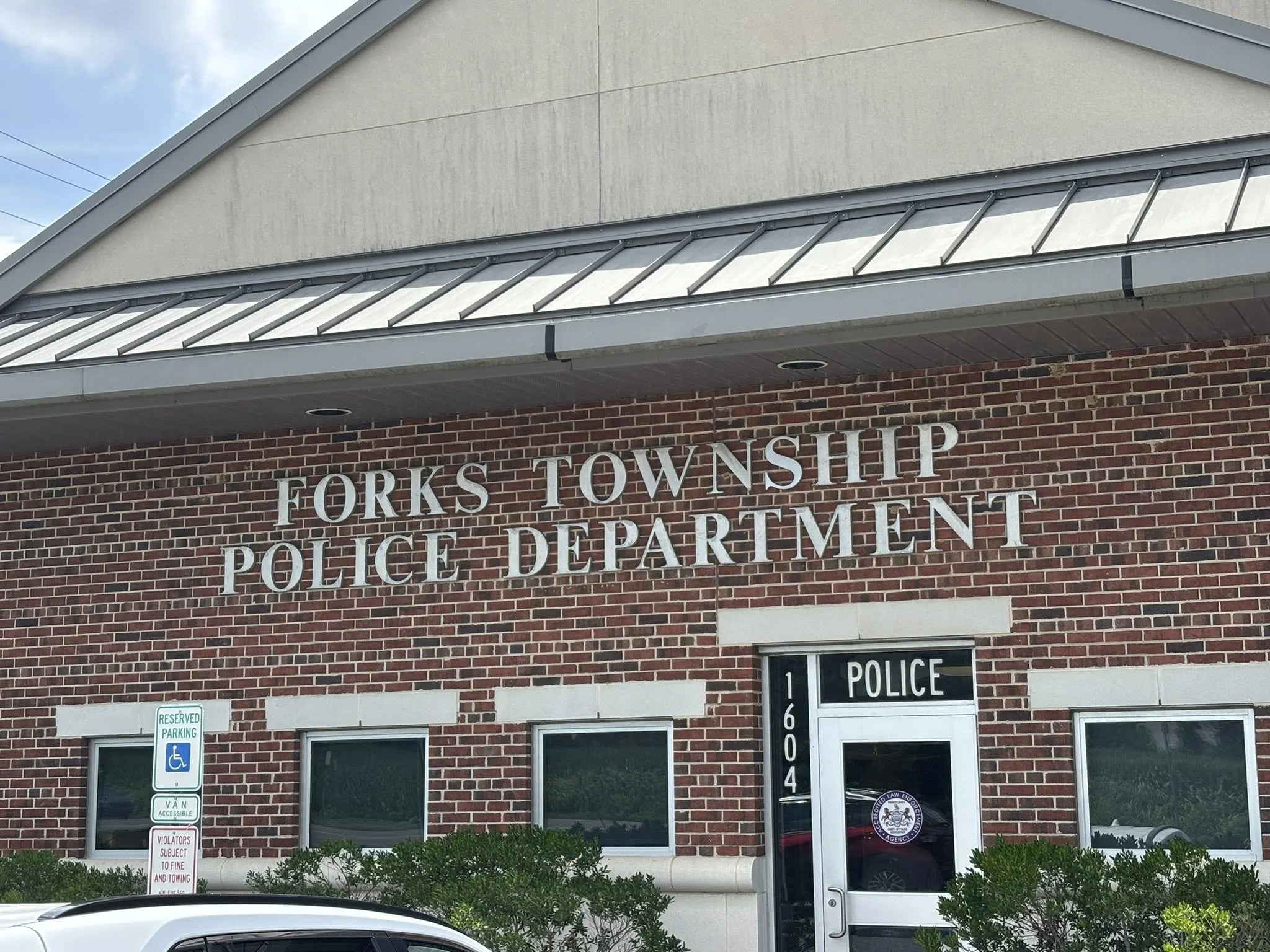 Exterior of a brick building labeled 'Forks Township Police Department' with a glass door, windows, and a reserved parking sign outside.