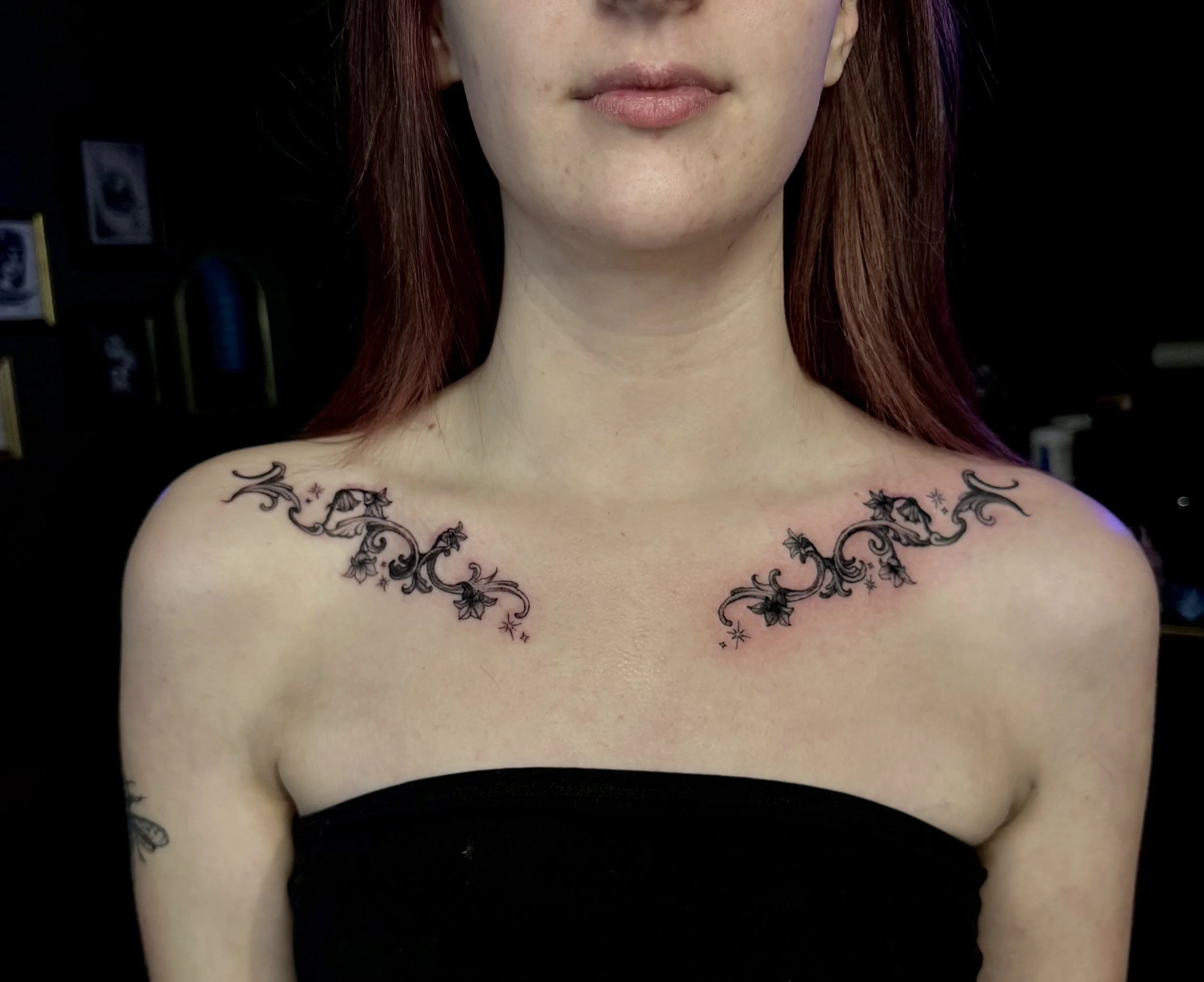 Close-up of a woman's upper chest with a floral tattoo across her collarbones, wearing a black strapless top.