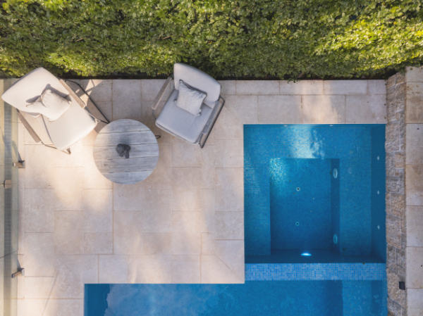 Aerial view of a backyard pool area with two white lounge chairs, a small round table, and a hedge along the back.