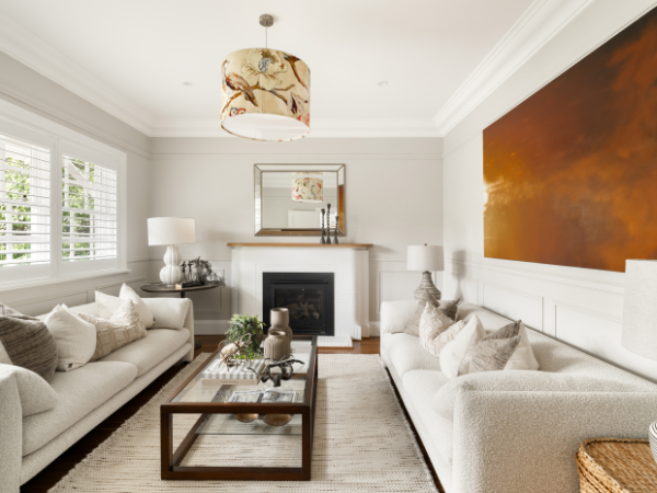 Living room with two white sofas, a glass coffee table, a fireplace, and a large orange painting on the wall.