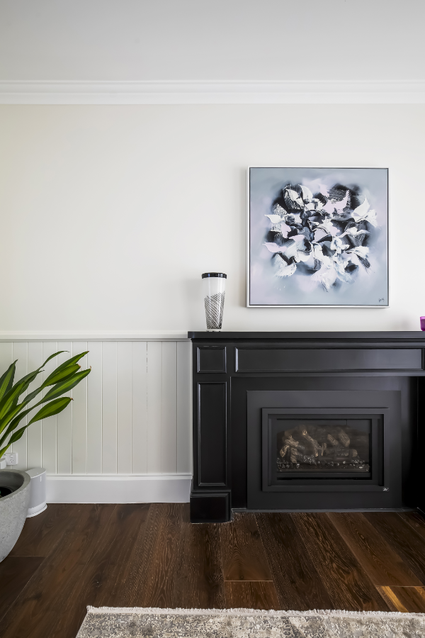 Living room with a black fireplace, abstract floral art, a tall decorative jar, a potted green plant, and hardwood floors.