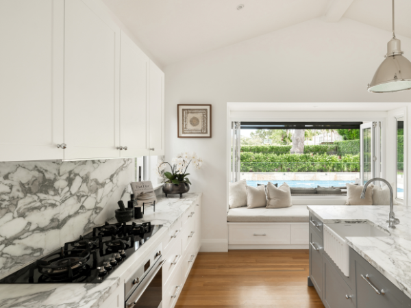 Kitchen with white cabinets, marble countertops, and a window seat overlooking a backyard pool