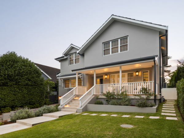 Front view of a modern gray two-story house with a porch, stairs, and a well-maintained lawn with stepping stones and shrubs.