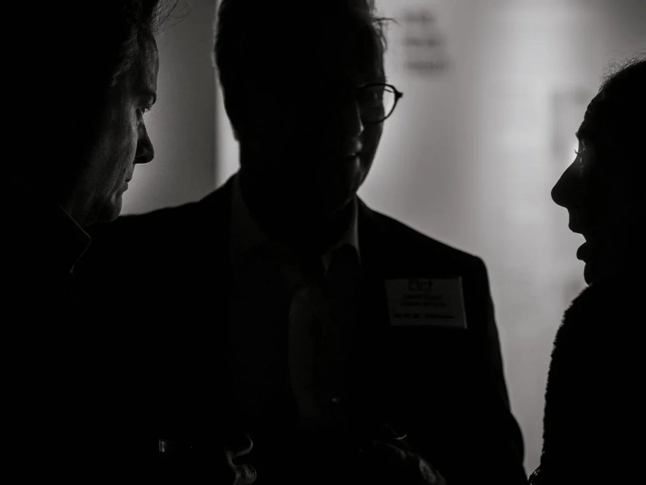 Silhouettes of three people engaged in conversation in a dimly lit setting.