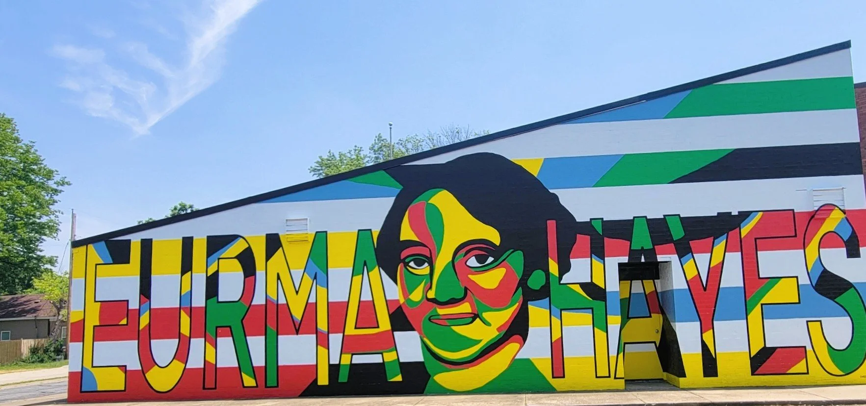 Mural in Southern Illinois nonprofit community arts mural project, independent artists, Carbondale, IL, Ecuadorian Lives in large, multicolored letters. Portrait of Eurma C. Hayes on the Eurma C. Hayes Community Center in Carbondale, IL.