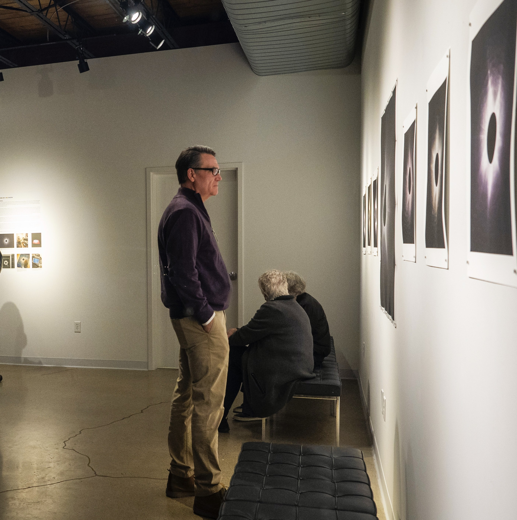 People observing artwork in an art gallery with white walls and framed photos or prints.
