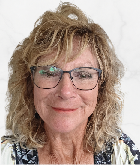 A smiling woman with gray hair holding a glass of pink beverage at a social event, wearing a red blazer and a lanyard.