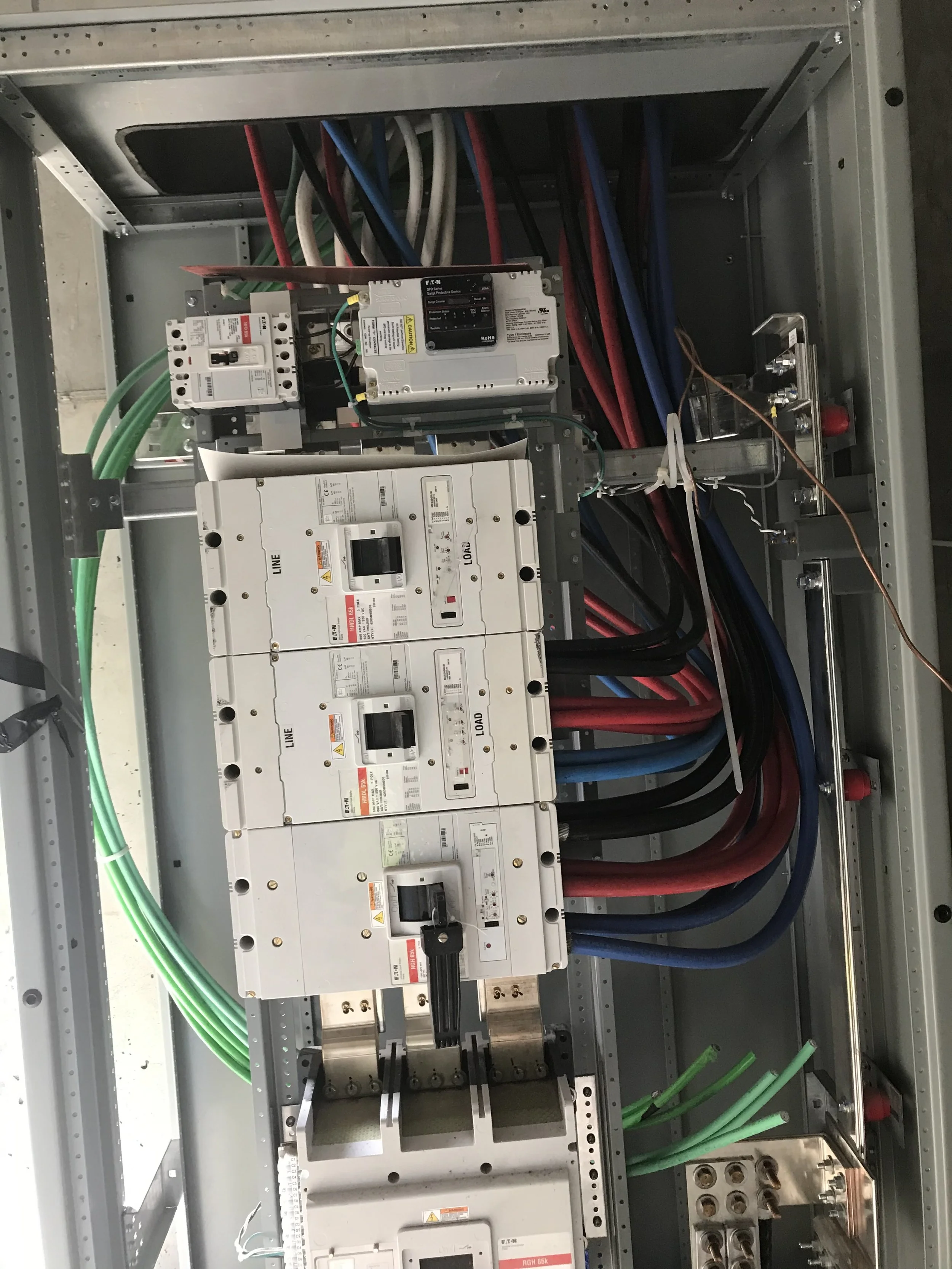 An open electrical panel with circuit breakers, wires, and electrical components inside.