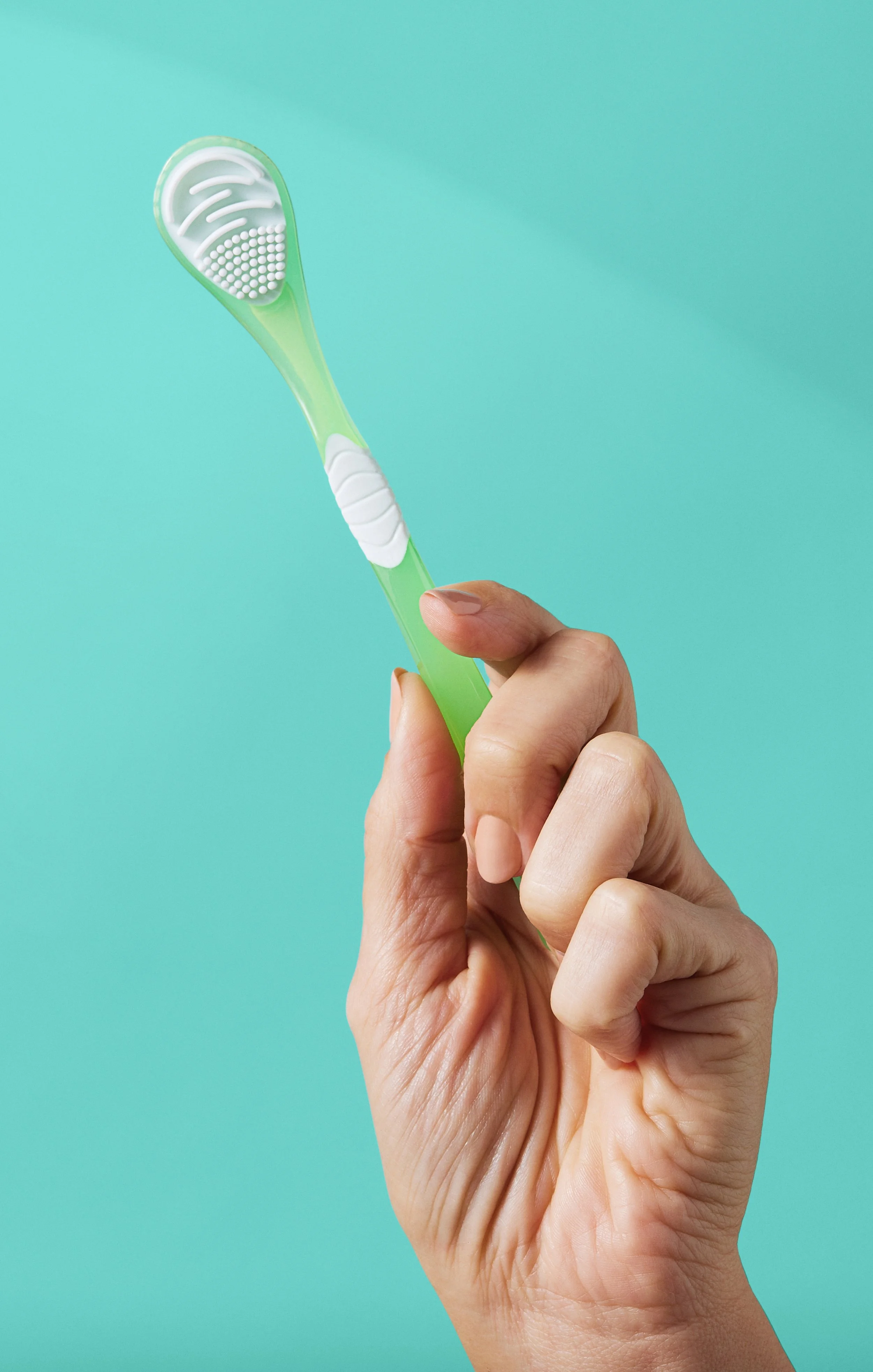 A hand holding a green toothbrush against a turquoise background.