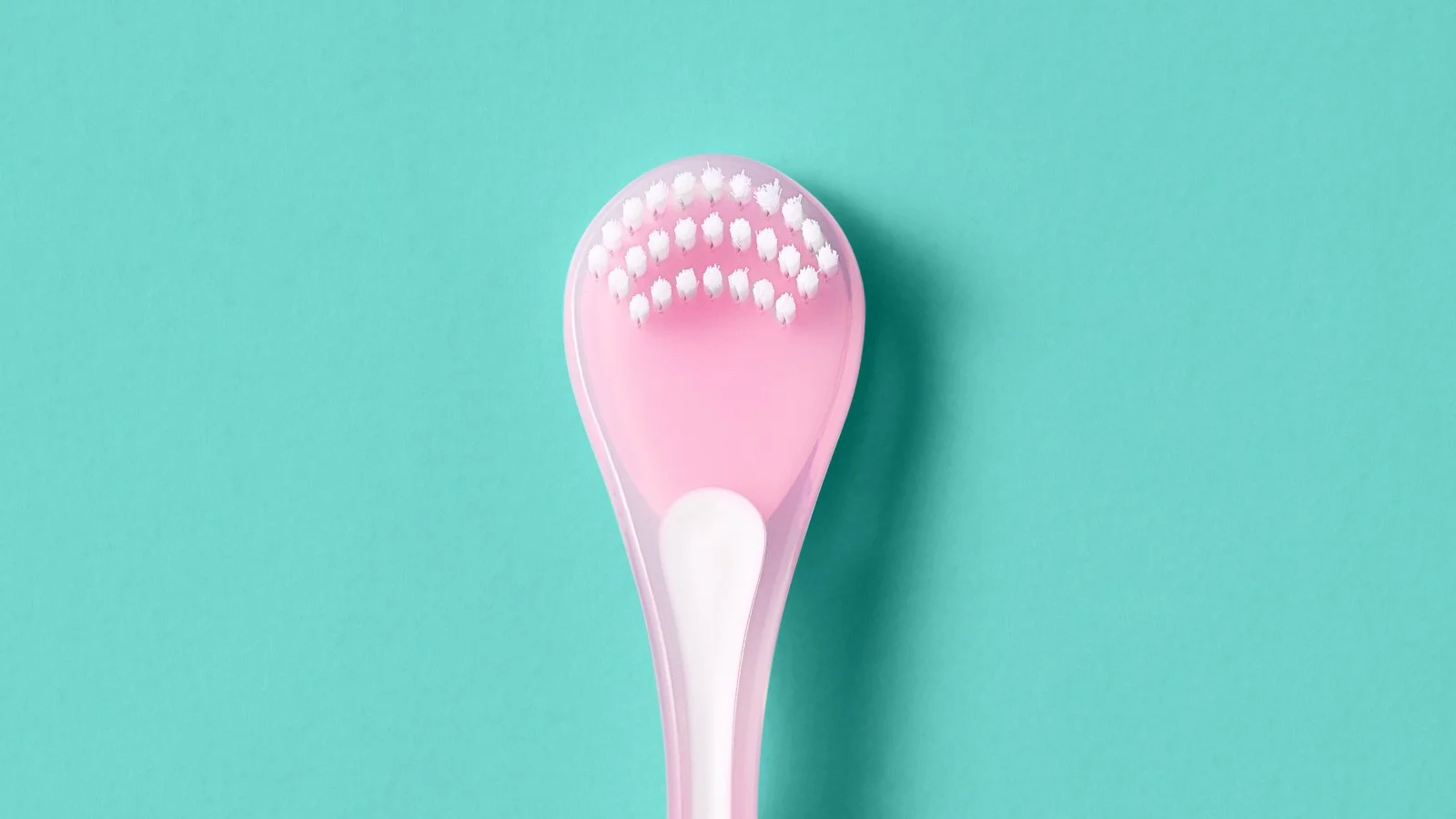 A pink and white exfoliating brush with white bristles on a turquoise background