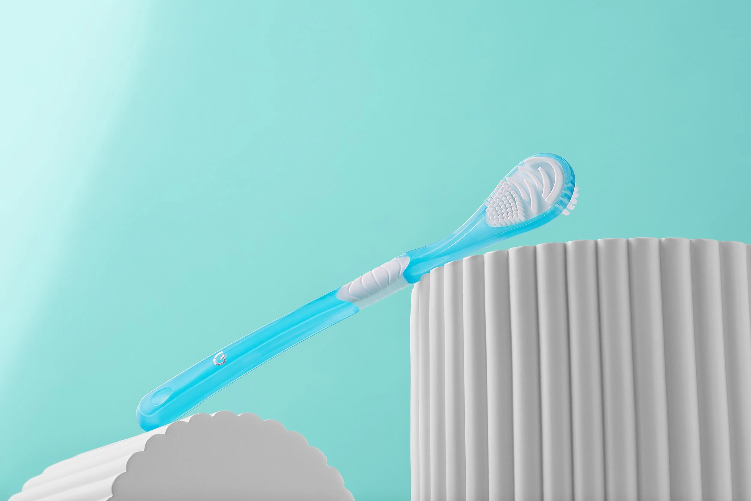 A blue toothbrush resting on a ridged white surface with a light blue background.