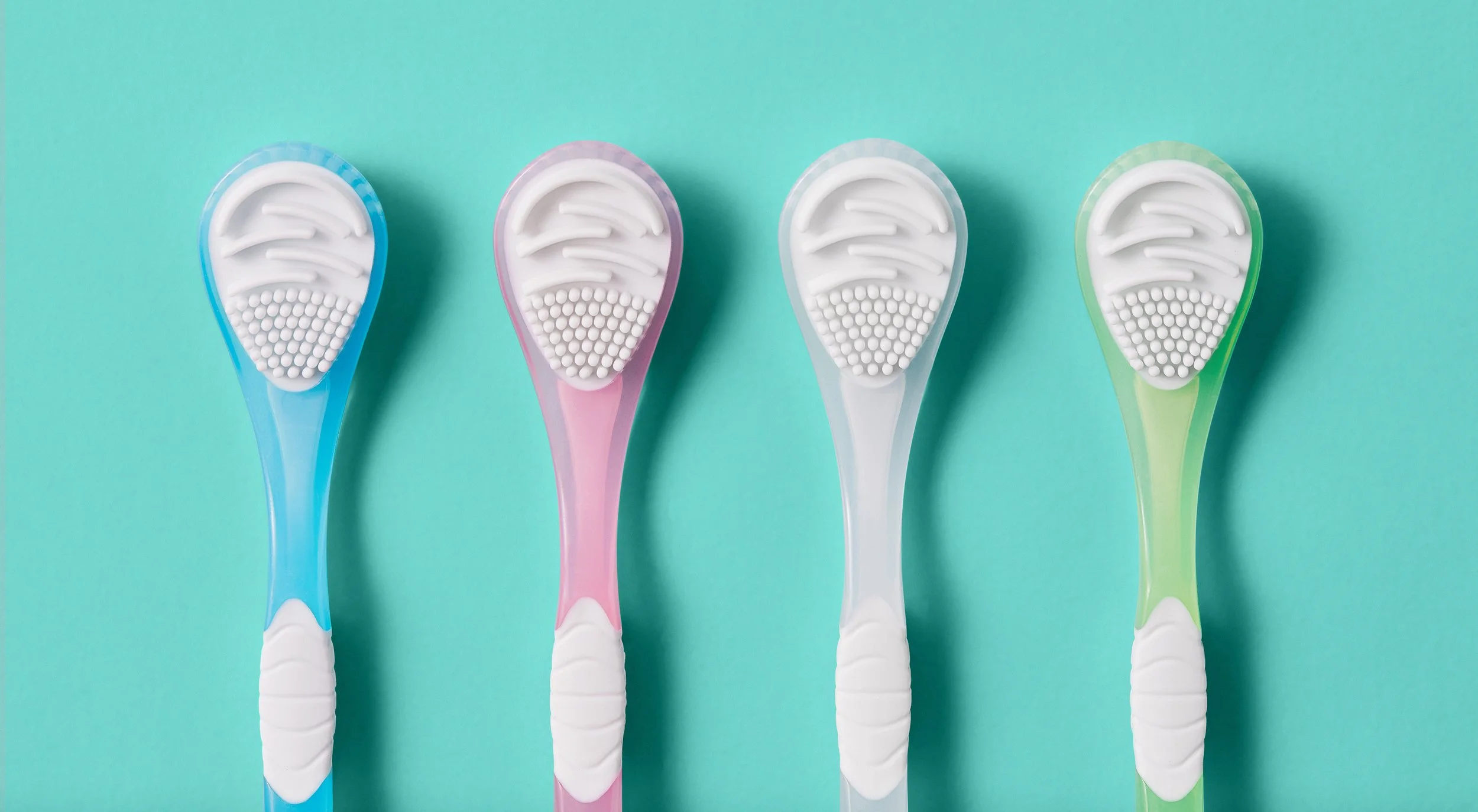 Four colorful toothbrushes with white bristles laid out on a light teal background.