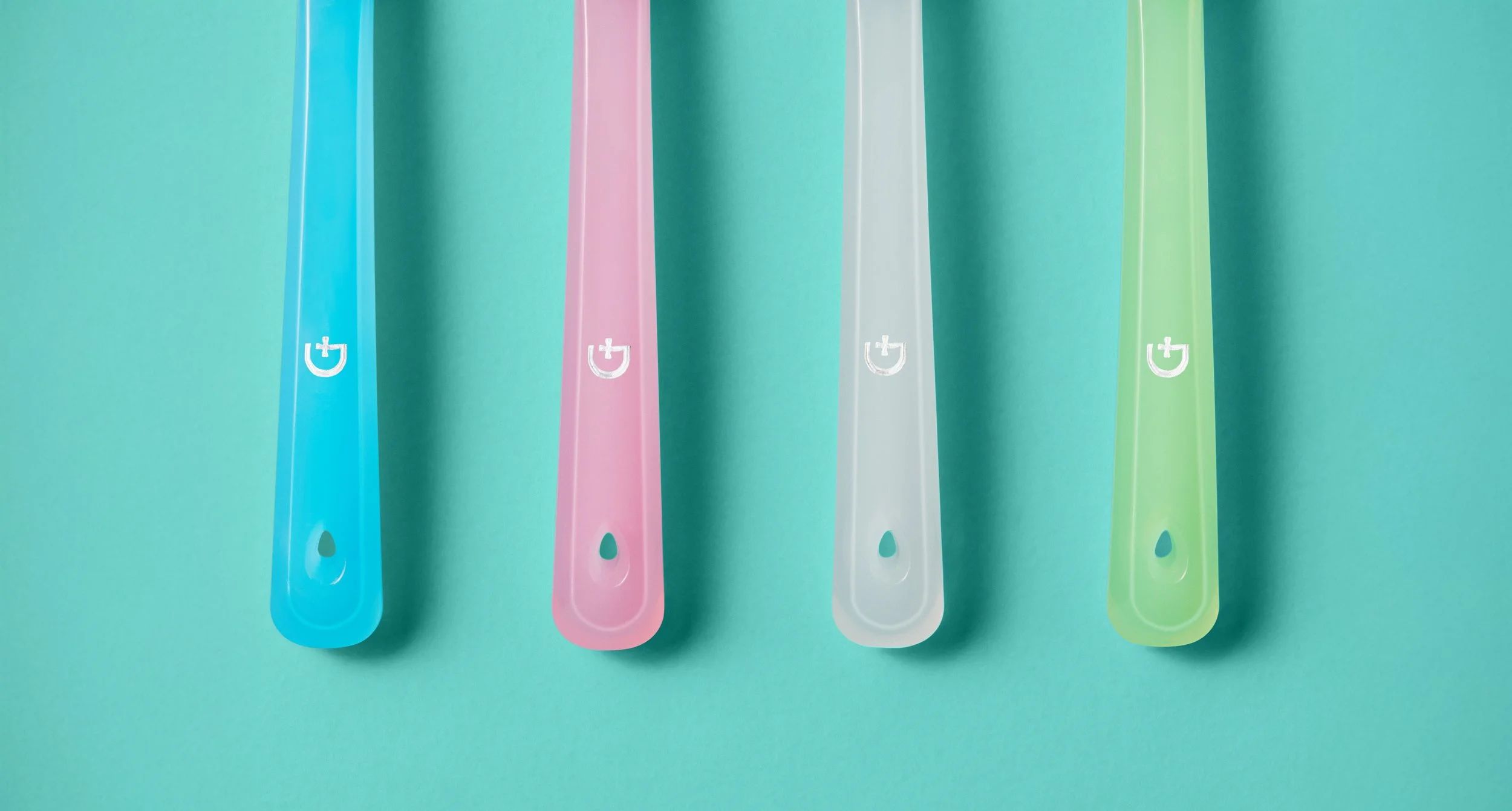 Four toothbrushes in blue, pink, clear, and green, arranged vertically on a mint green background.