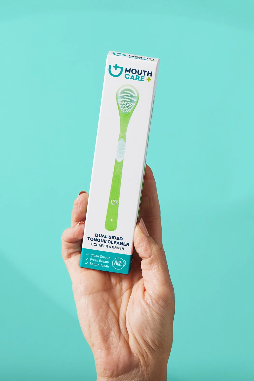 A hand holding a box of Mouth Care's dual-sided tongue cleaner with a scraper and brush, against a blue background.