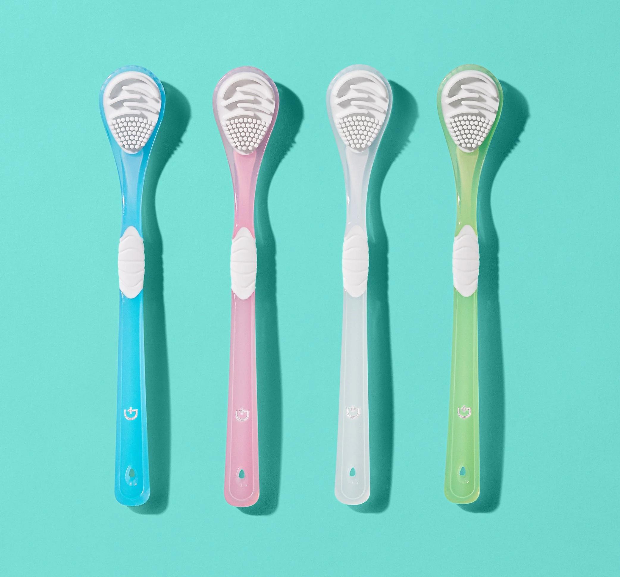 Four colorful toothbrushes in blue, pink, white, and green on a turquoise background.