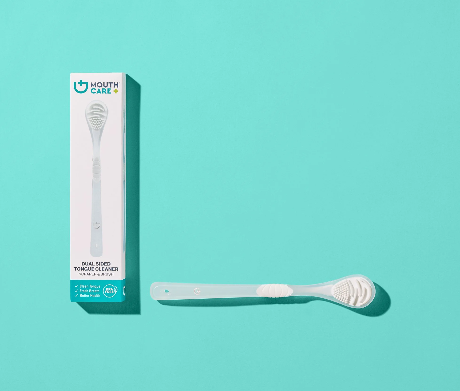 A white dual-sided tongue cleaner scraper and brush lying on a turquoise background next to its packaging box, which features an image of the tongue cleaner and product information.