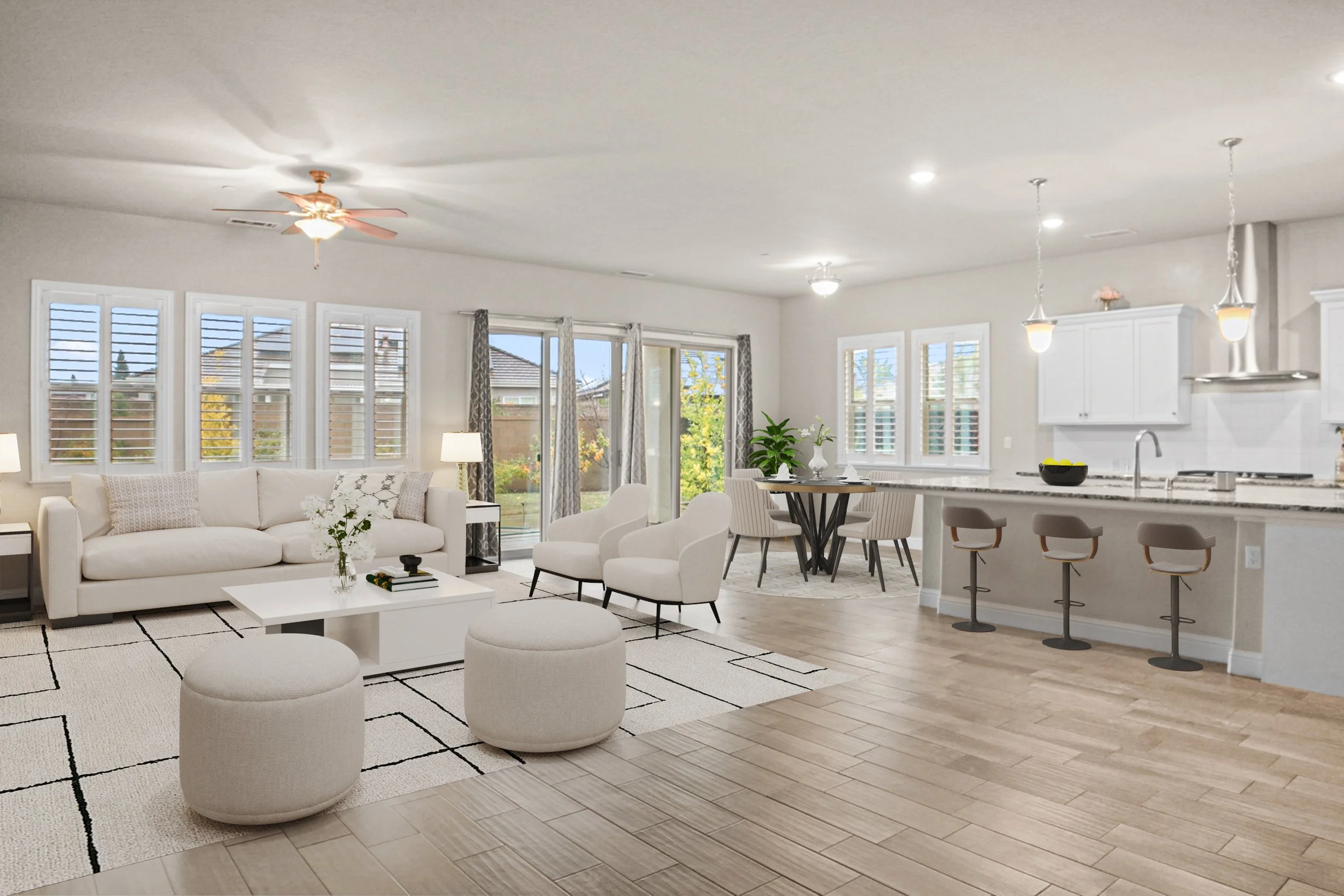 Bright, modern open-concept living room and kitchen with white furniture, wooden flooring, large windows with plantation shutters, sliding glass door, and decor including plants and vases.