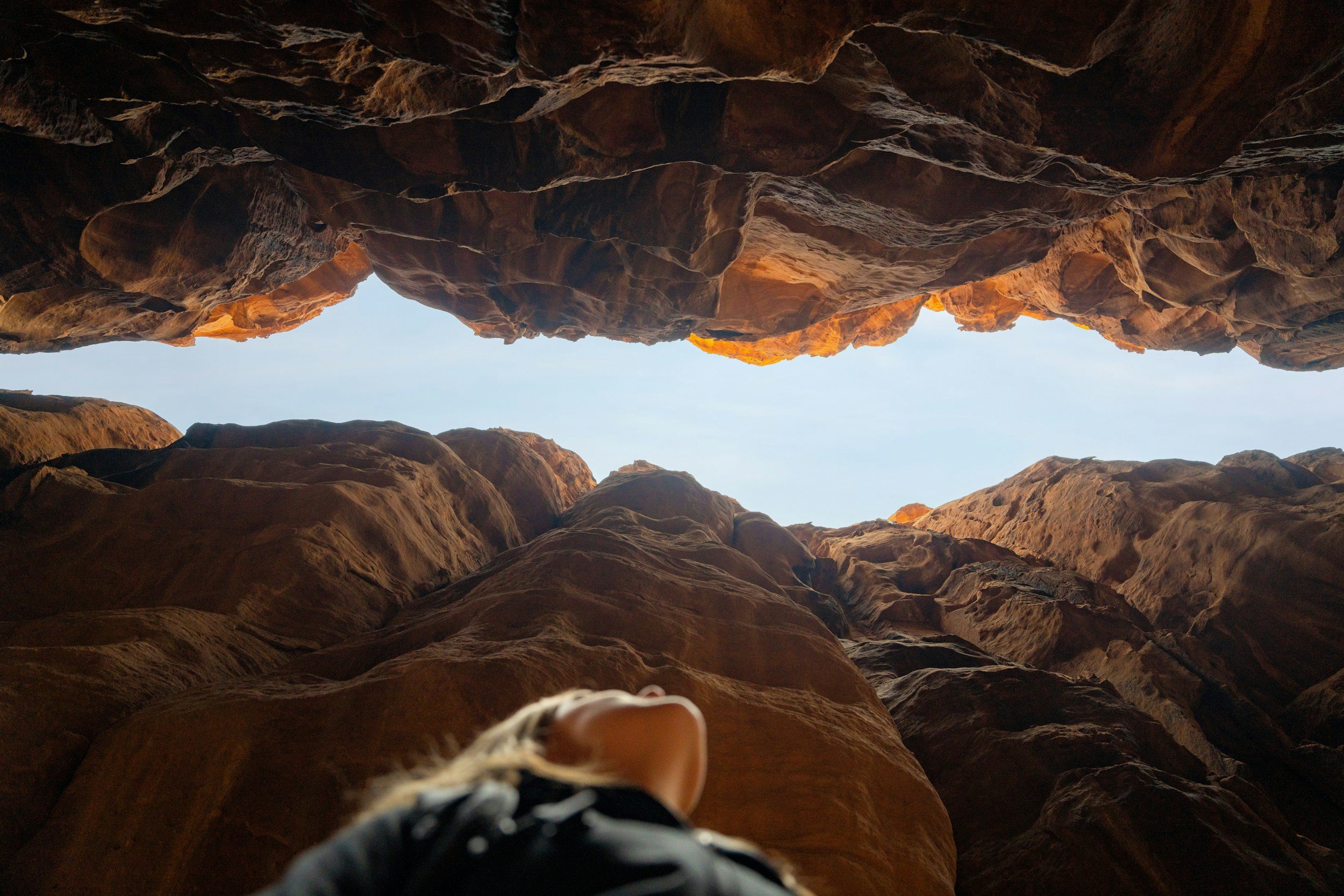 Looking up through a narrow canyon at the blue sky and a person's head and shoulder in the foreground.