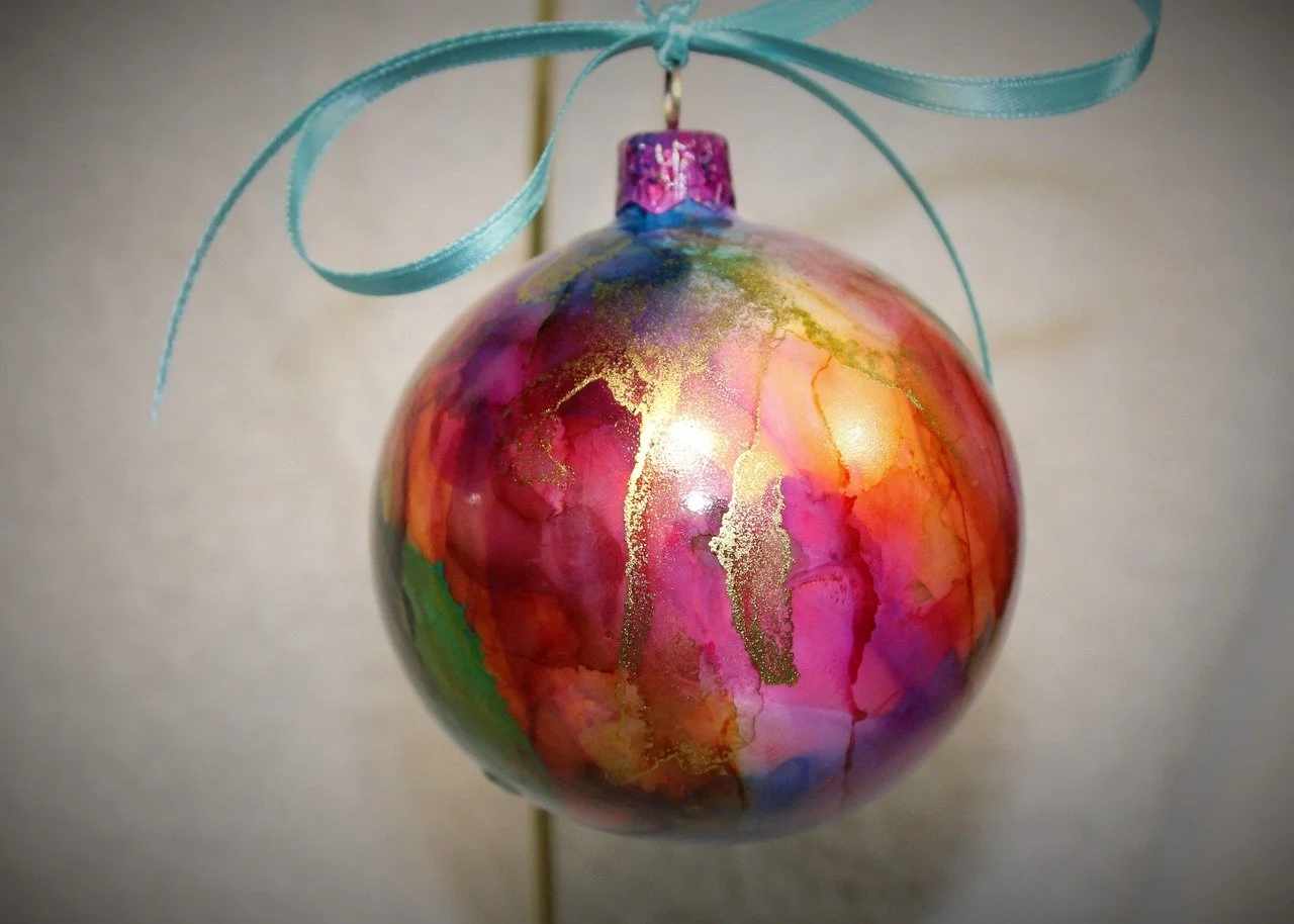Christmas ornament painted inside with pink, orange, and gold alcohol inks and tied with a blue ribbon