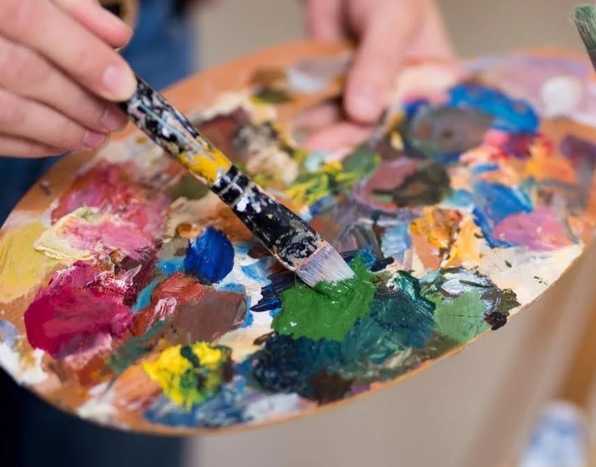 Artist mixing oil paint colors on a wooden palette with a brush