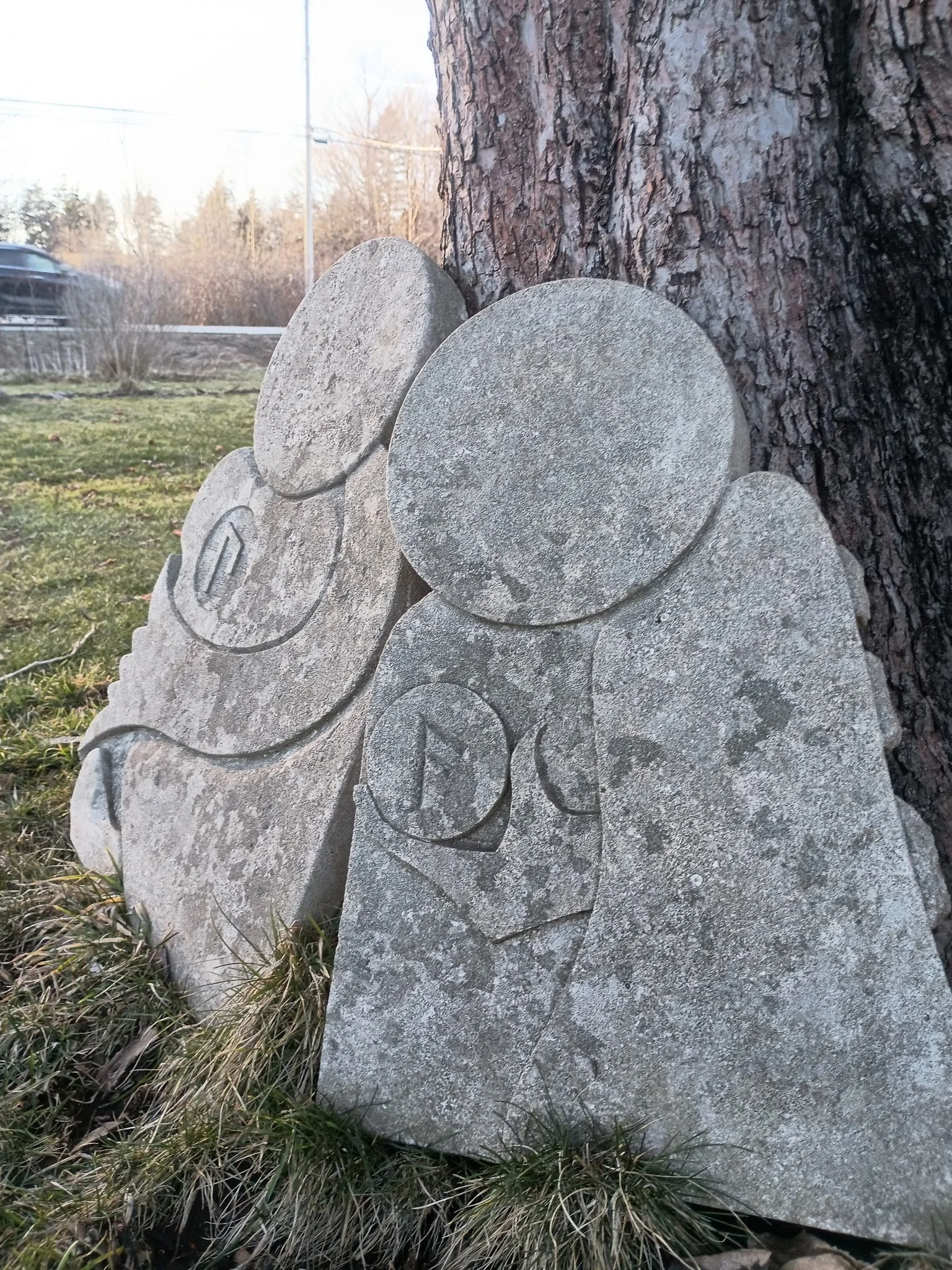 Stone sculpture of a family, depicting two adults and two children, sitting against a tree outdoors.