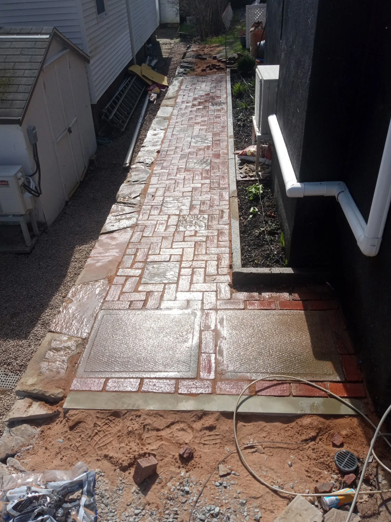 Newly paved brick sidewalk alongside a house with construction materials and tools nearby.