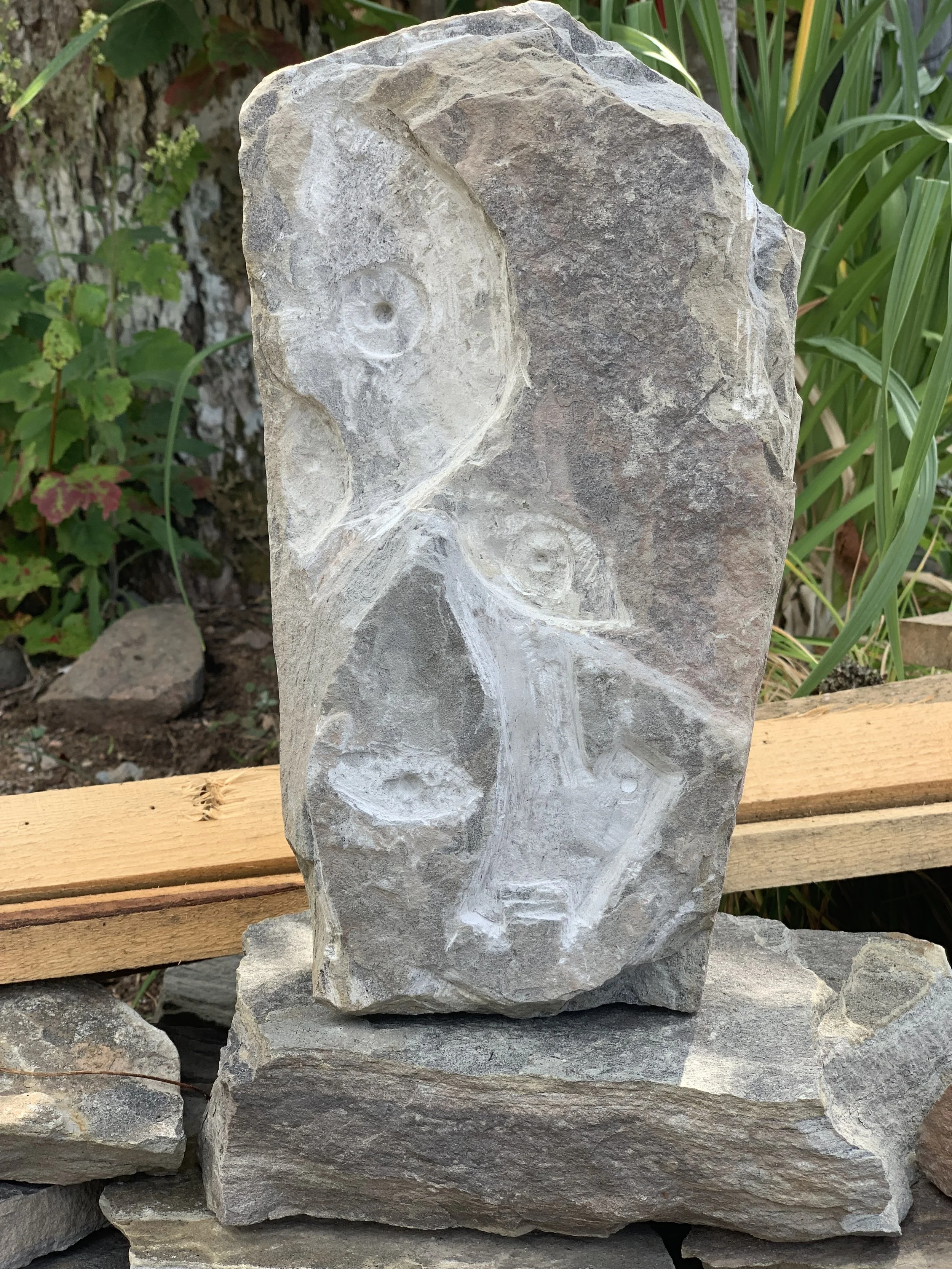 A stone with a strange face with many eyes carved into it.