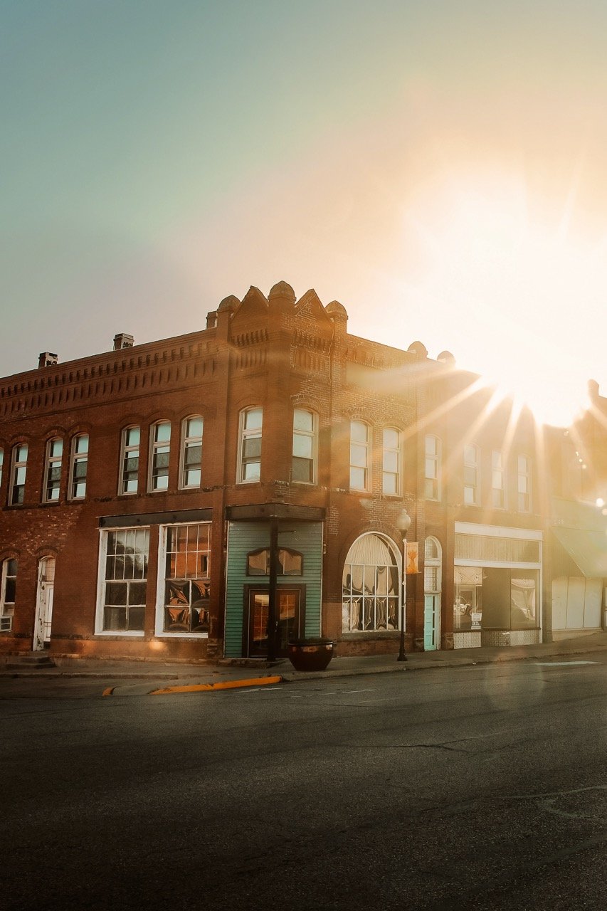 Sunset over a brick building on a city street with empty sidewalk and lamp post.