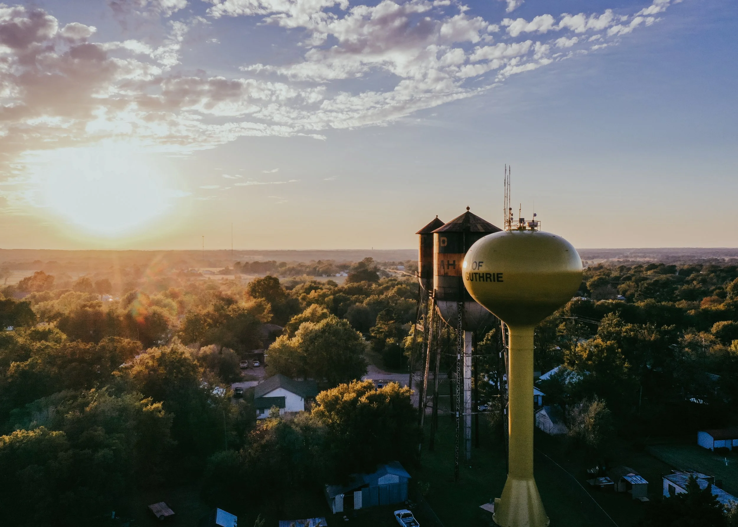 Sunset over a rural area with water towers and trees.