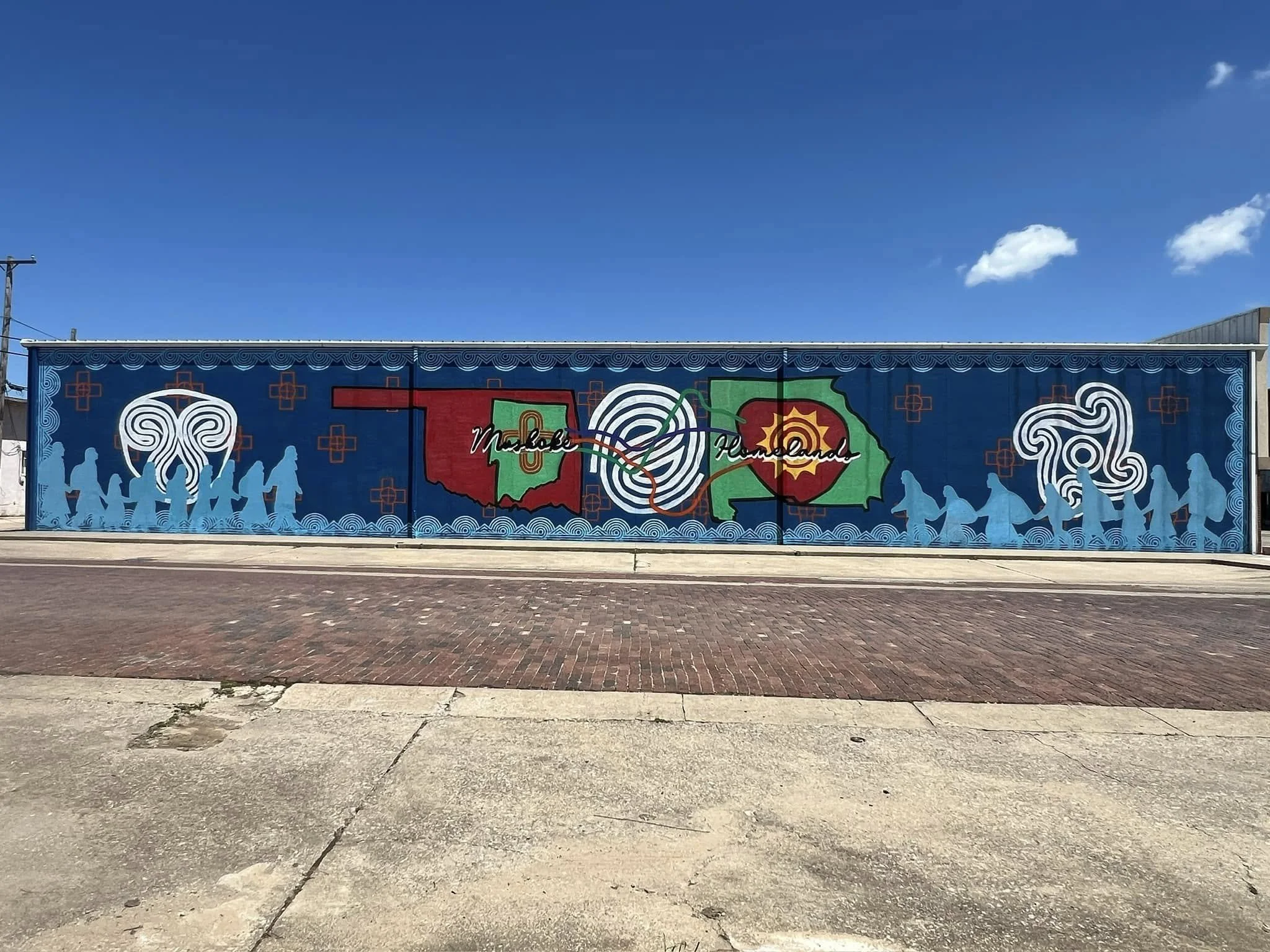 Colorful mural featuring symbols of Oklahoma and Hawaii, with the words 'Muskogee' and 'Hawaii' and illustrations of people holding hands on both sides.