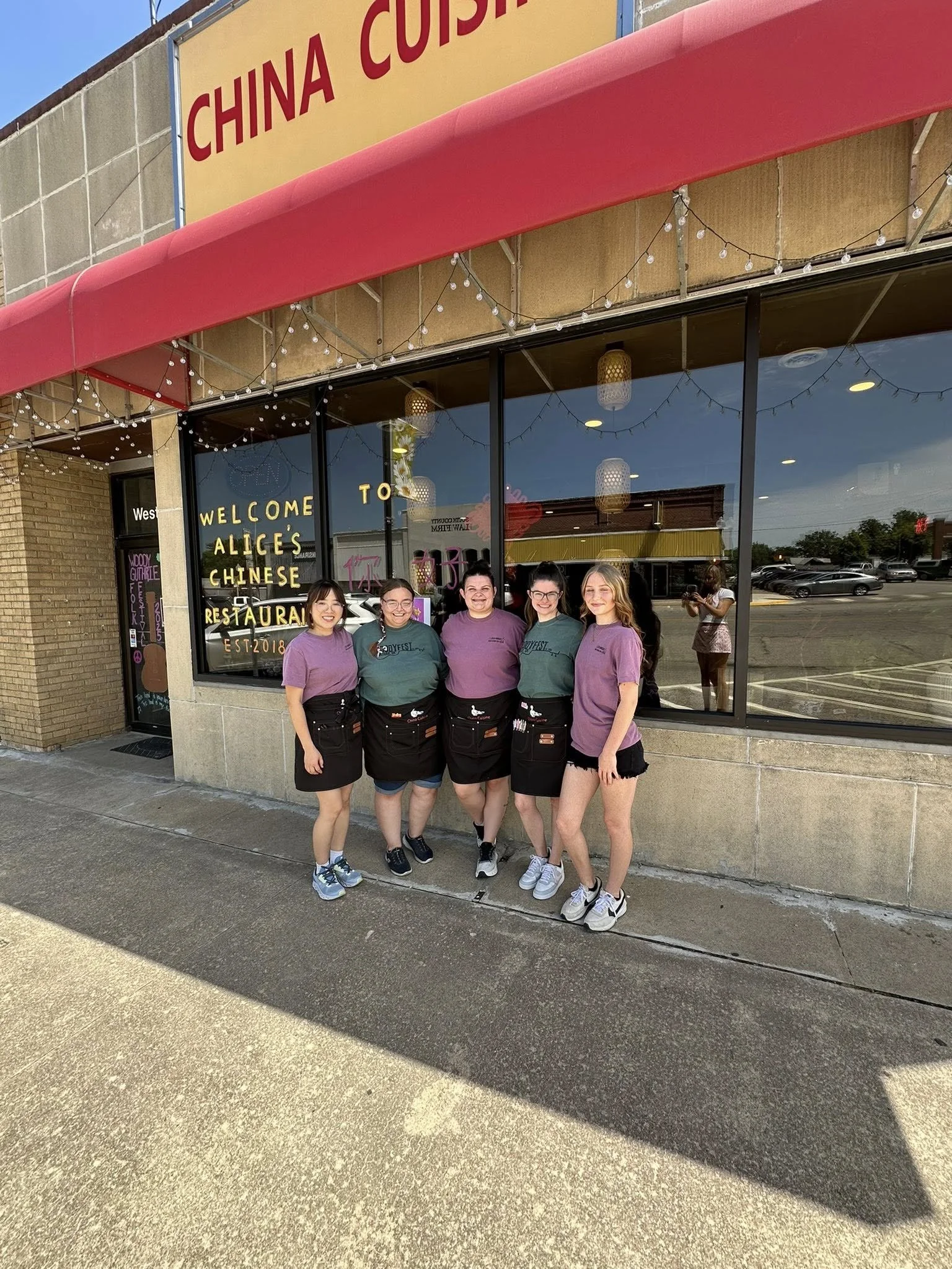 Five employees standing outside a Chinese restaurant called Alice's with a red awning and string lights, smiling for the photo.