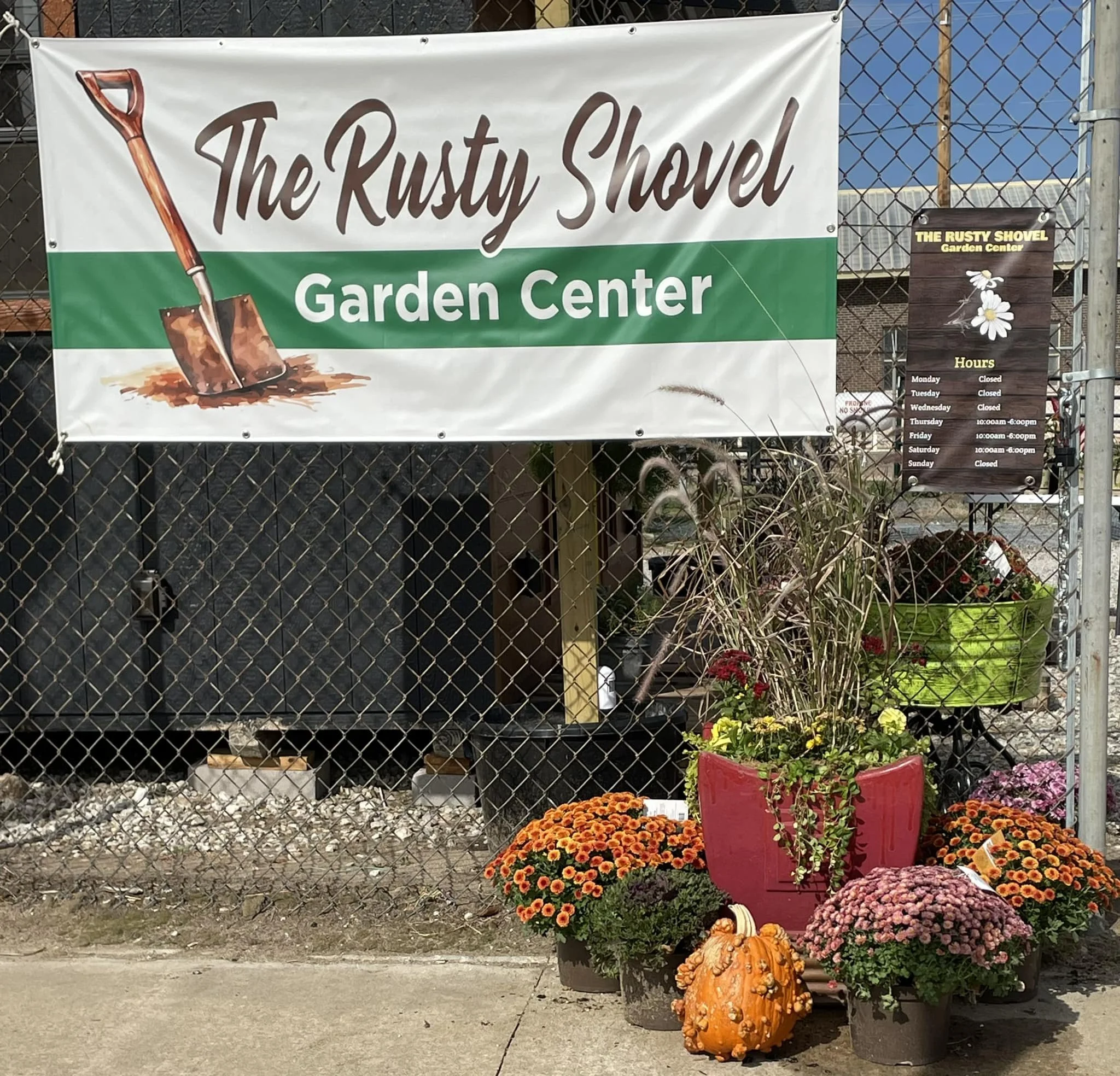 Flowers and a pumpkin outside the Rusty Shovel Garden Center with a sign displaying hours of operation.