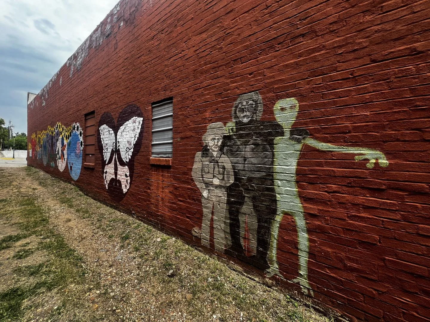 Colorful graffiti mural on a red brick wall featuring various characters, including two humanoid figures and a yellow alien figure with outstretched arm in front.