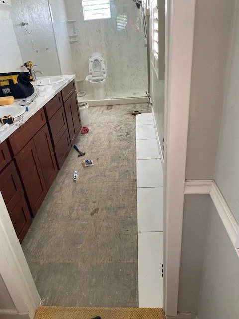 Bathroom with a partially cleaned floor, a vanity with tools on it, and a toilet in the background.
