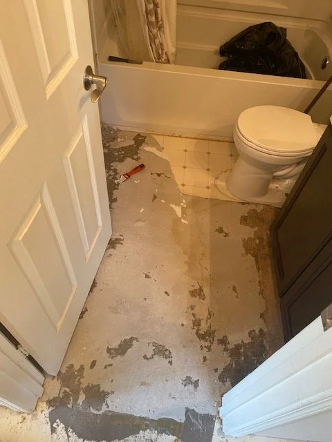 Bathroom with partially installed flooring, toilet, and a trash bag in the corner.