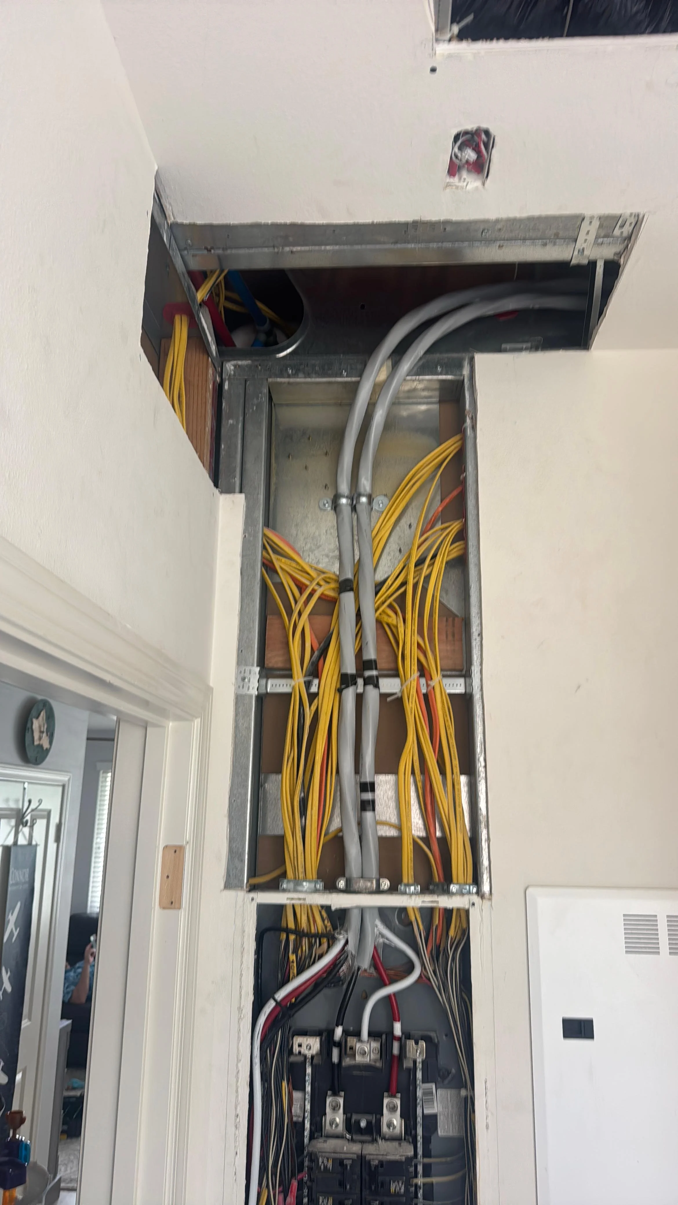 Before drywall repair showing an open electrical panel cavity with exposed wiring and unfinished wall framing that required proper enclosure and wall restoration.