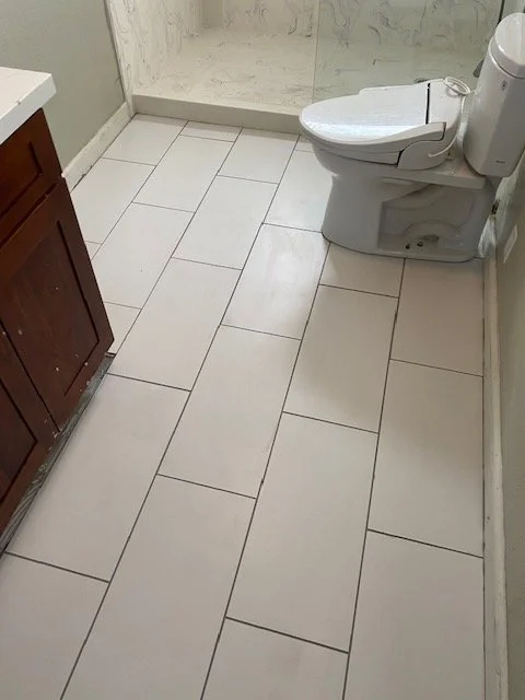 Bathroom with beige tiled floor, a wooden cabinet on the left, and a white toilet on the right.