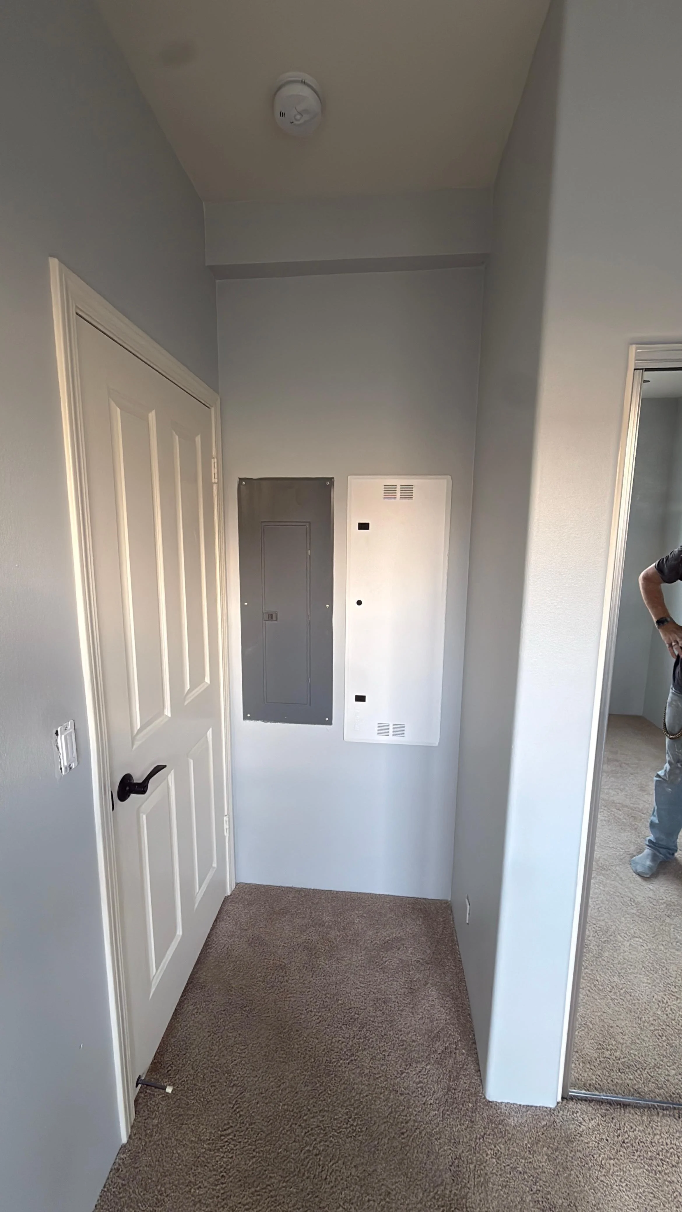 After drywall repair and wall finishing with the electrical panel fully enclosed, clean access doors installed, and the hallway restored to a smooth, finished, code-ready appearance.