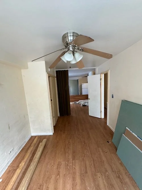 Empty room with a ceiling fan, hardwood floor, and construction materials leaning against the wall.
