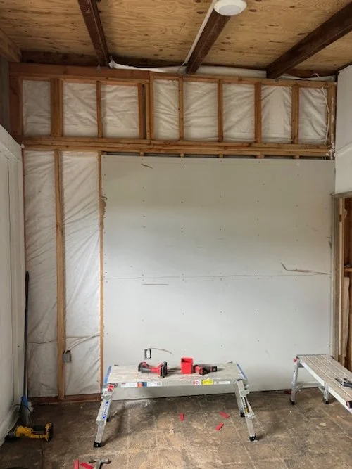 Room under renovation with exposed wooden framing, insulation, and construction tools on a workbench.