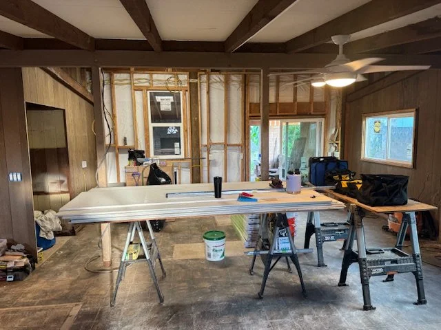 Interior of a room under construction with exposed wooden framing, a workbench with tools, and a ceiling fan.