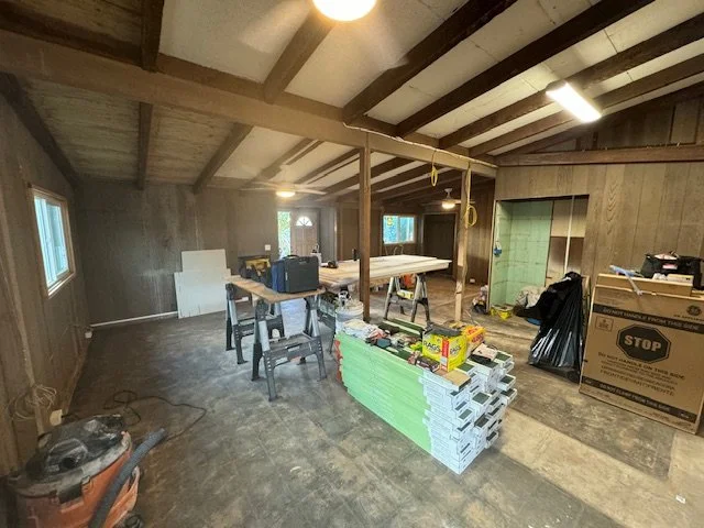 Interior of a room under renovation with construction materials, tools, and furniture scattered around.