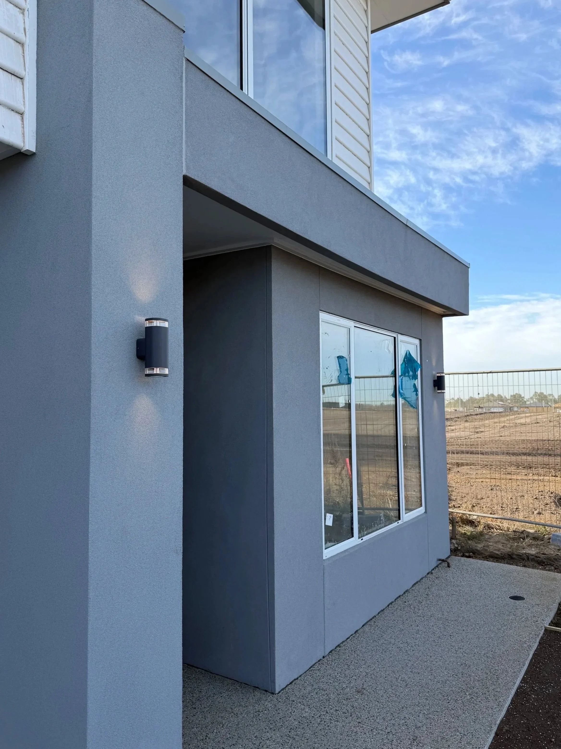 Under construction house with scaffolding and blue weather-resistant building wrap, blue tarp covering materials, and a clear sky with white clouds.
