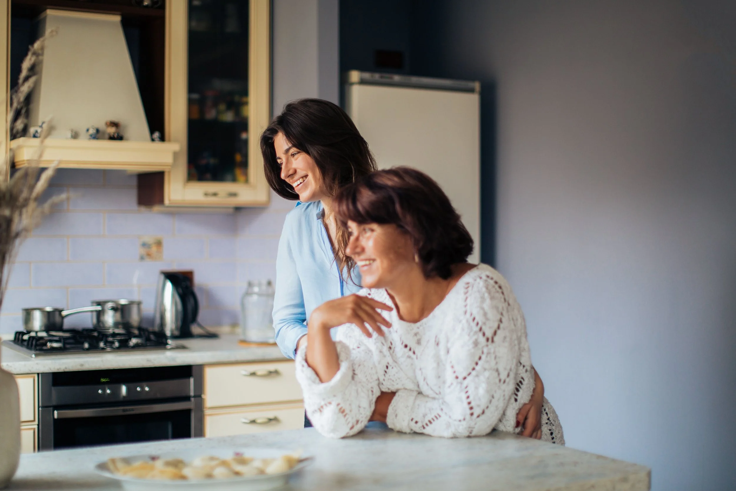 A mother and daughter sharing a happy moment in a modern kitchen, both smiling.