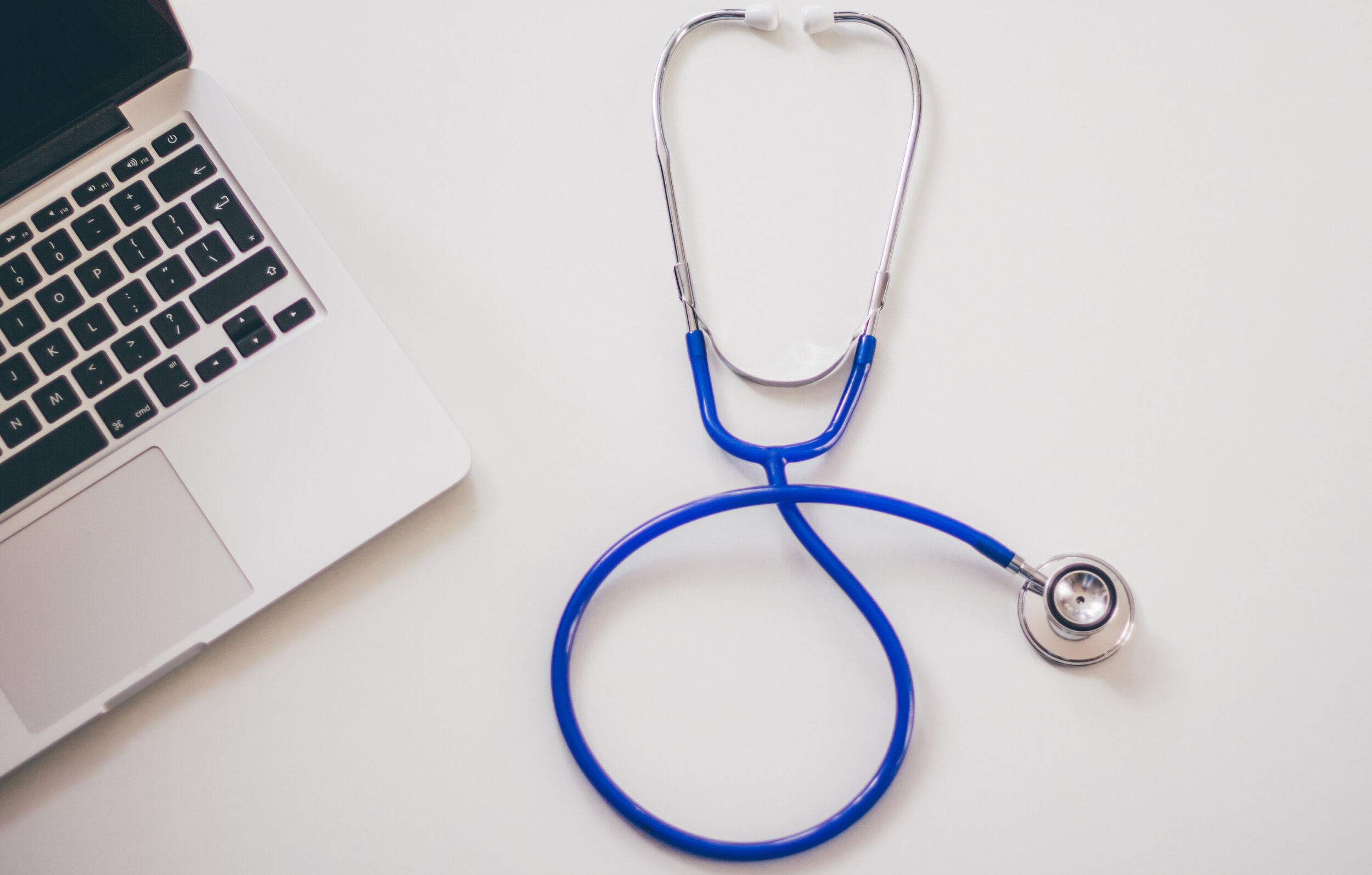 Laptop next to a blue stethoscope on a white surface.